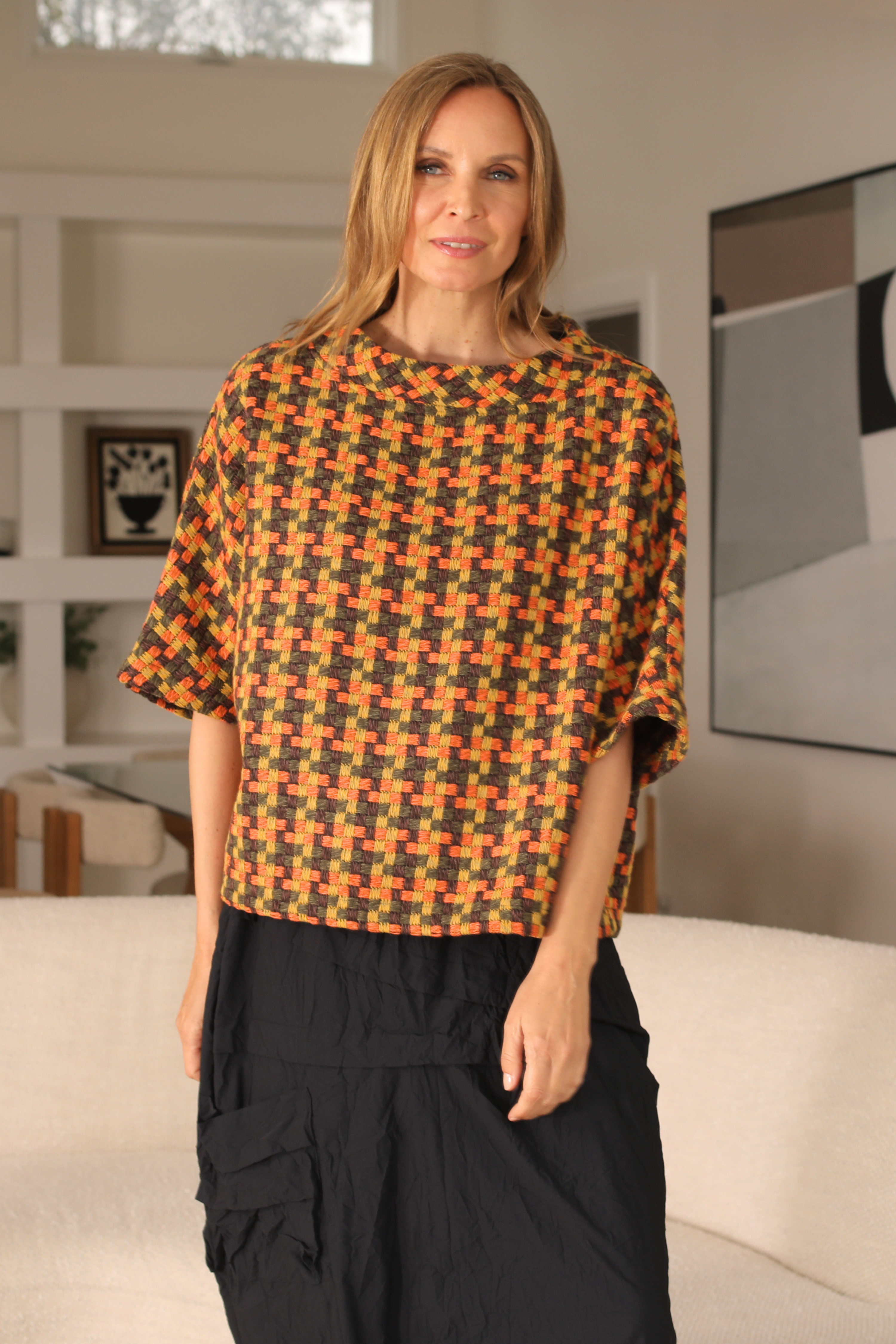 Woman wearing a patterned top and black pants in a living room setting