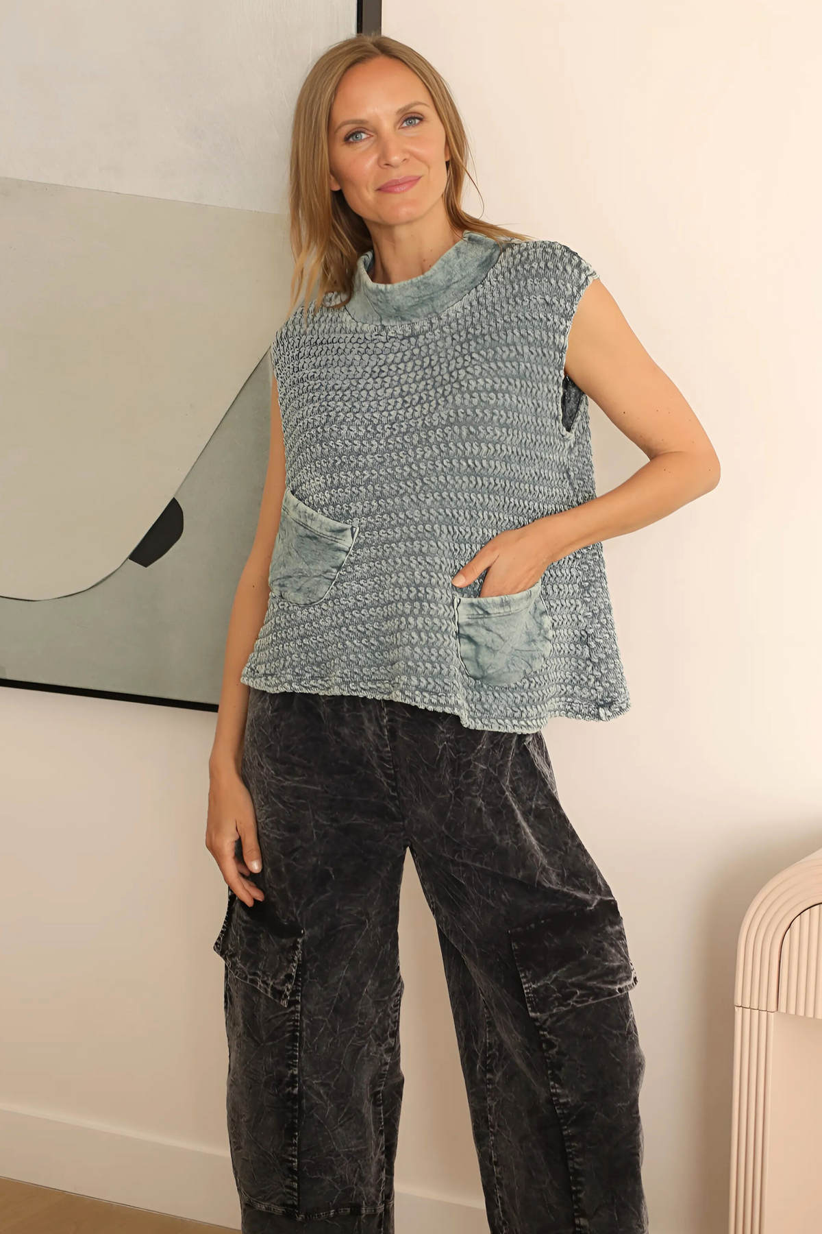 Woman wearing a sleeveless knitted top and black pants indoors.