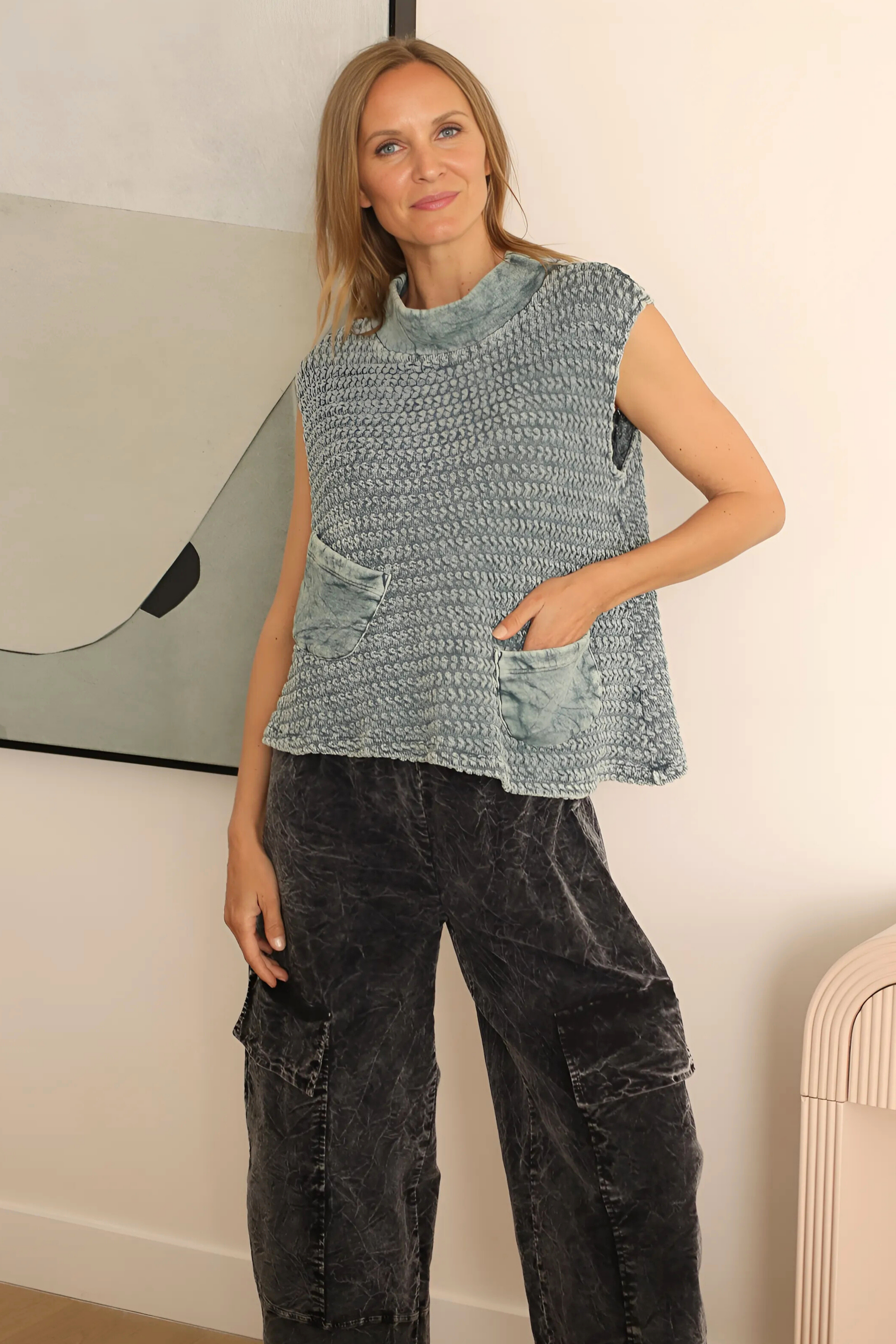Woman wearing a sleeveless knitted top and black pants indoors.