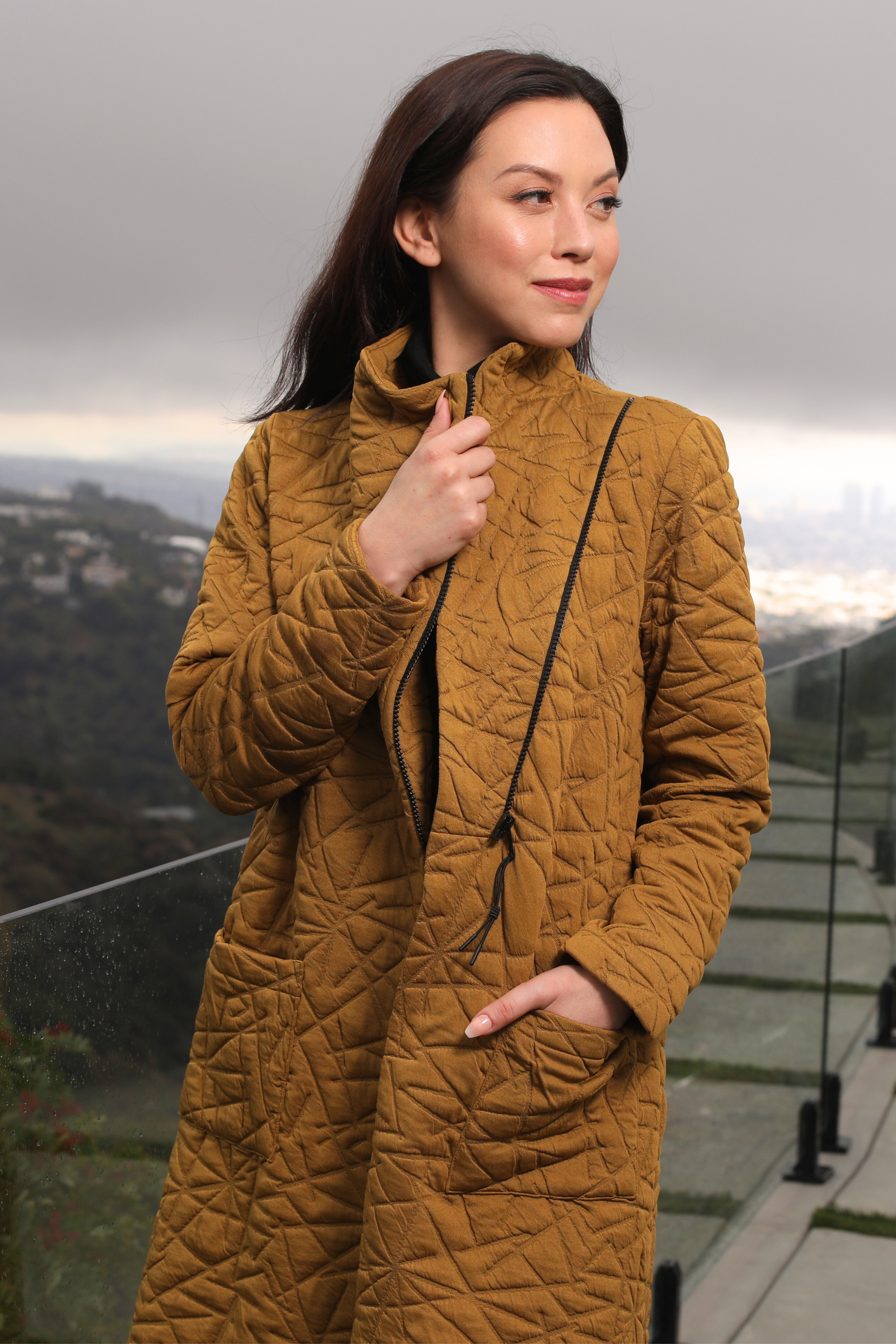 Woman wearing a mustard yellow quilted coat with a scenic background