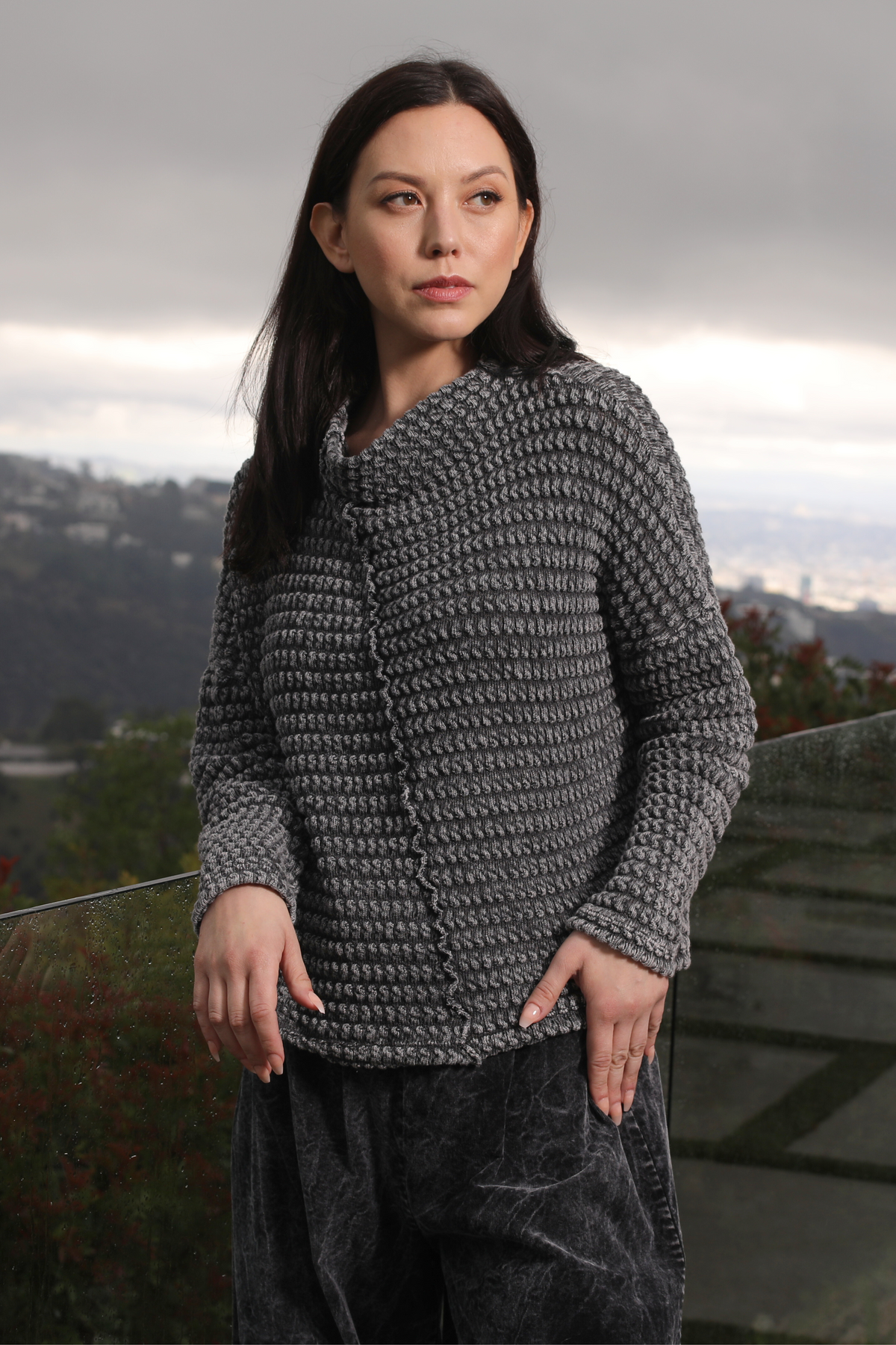 Woman wearing a textured gray sweater with a scenic background