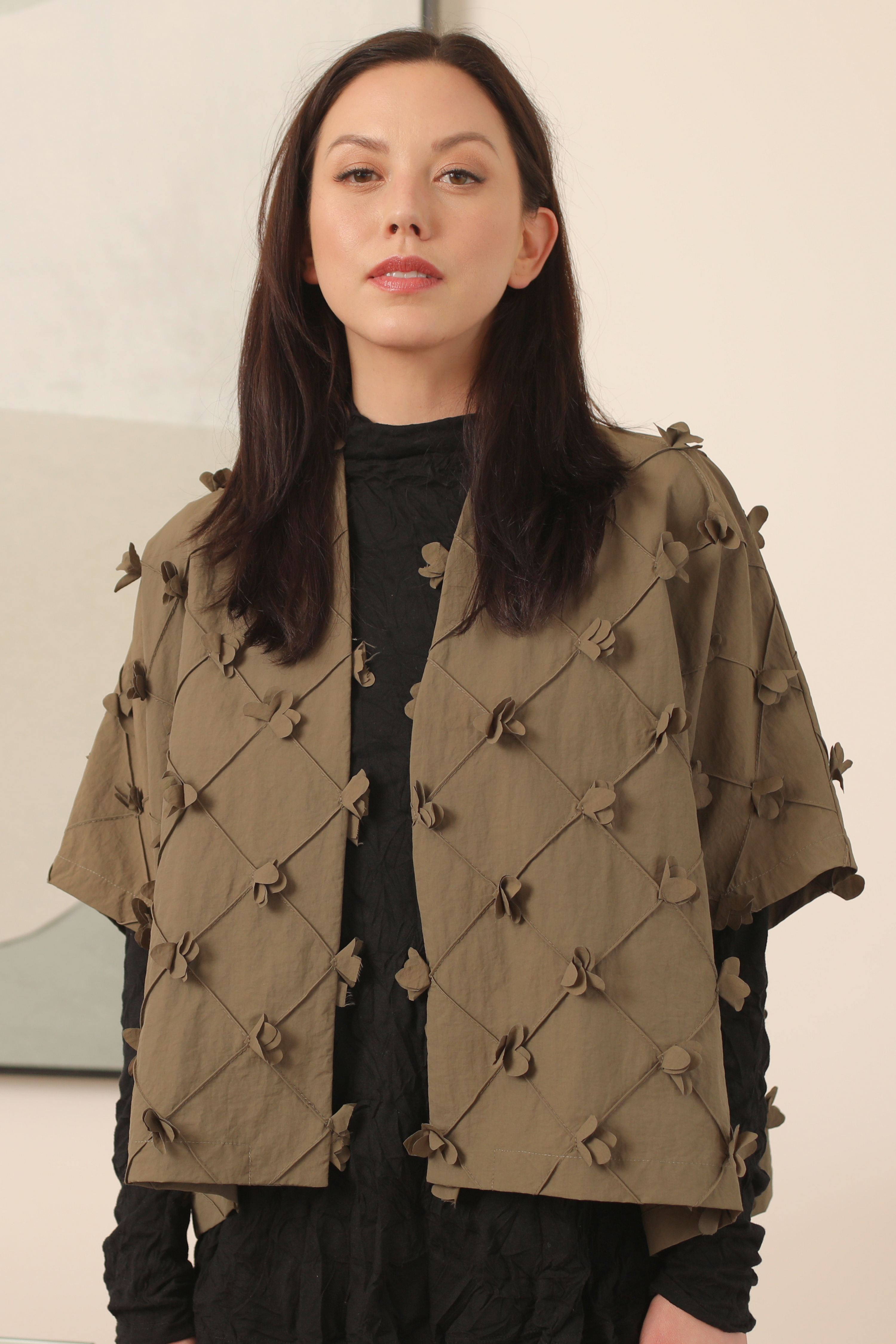 Woman wearing a green jacket with button details against a plain background