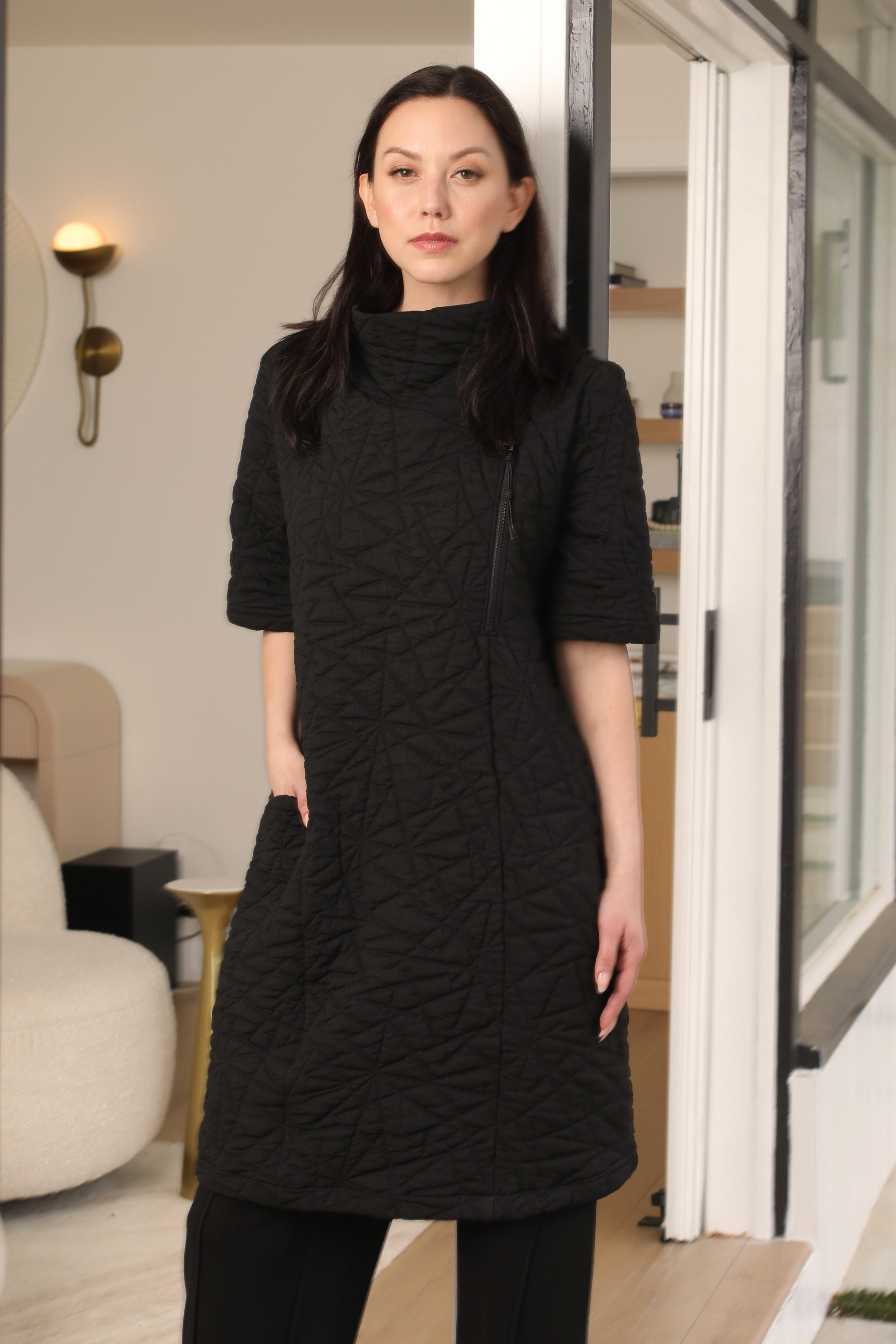 Woman wearing a black textured dress standing in a modern indoor setting.