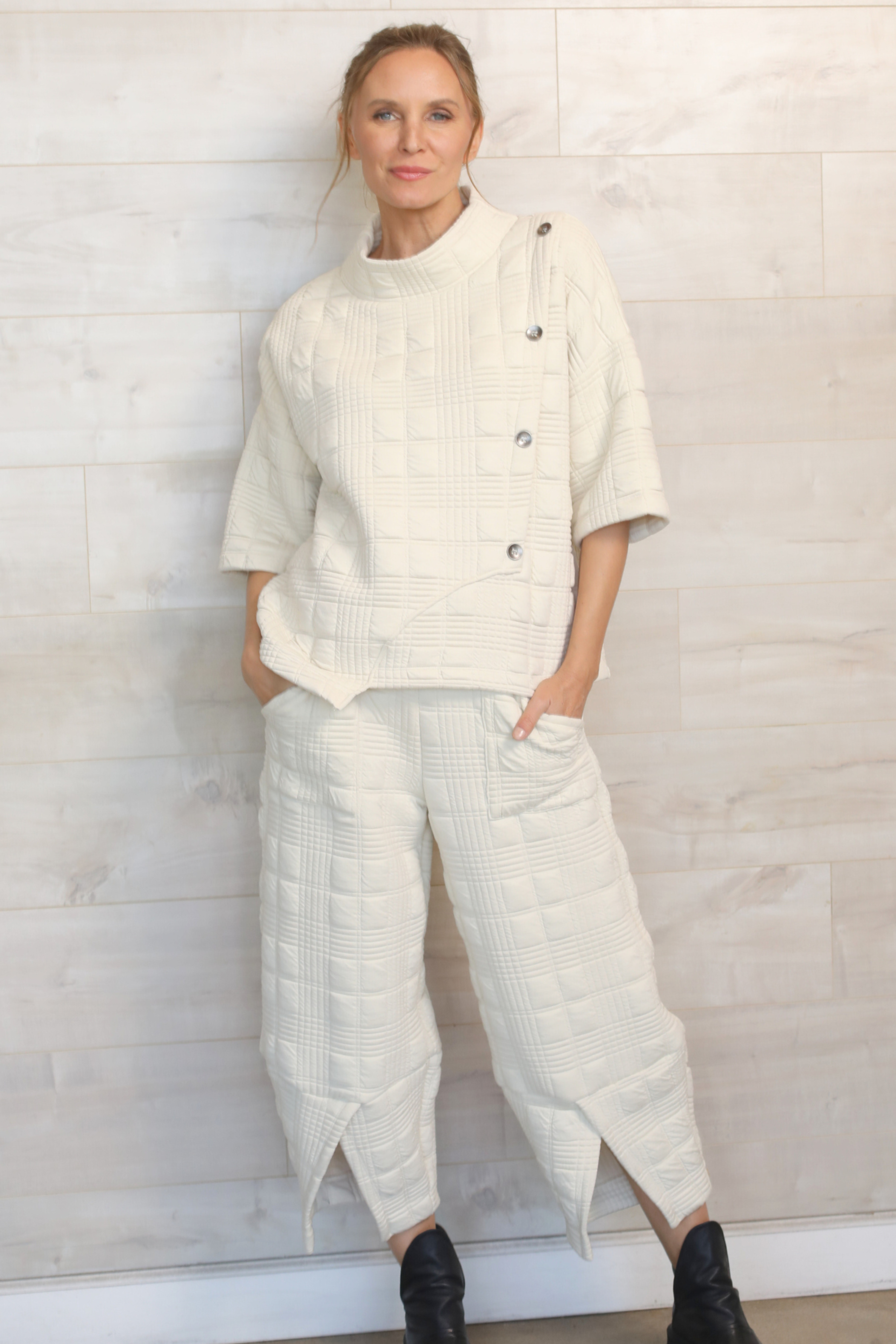 Person wearing a white outfit with a textured top and wide-leg pants against a light background